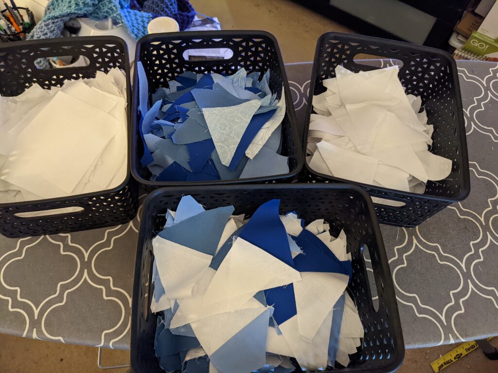 Four small bins filled with blue and white triangles and squares fabric, ready for piecing.