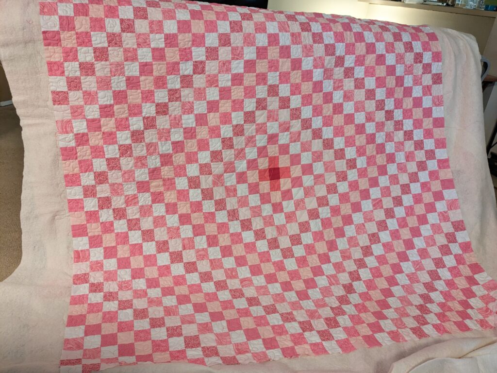 The fully quilted Around the World quilt in pink, after quilting, prior to being squared up and bound.