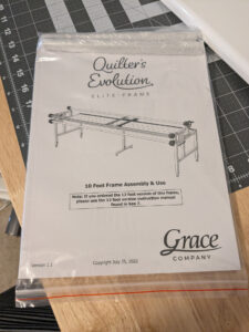 The instruction manual for the Quilter's Evolution Elite frame in it's bag, sitting on a table.
